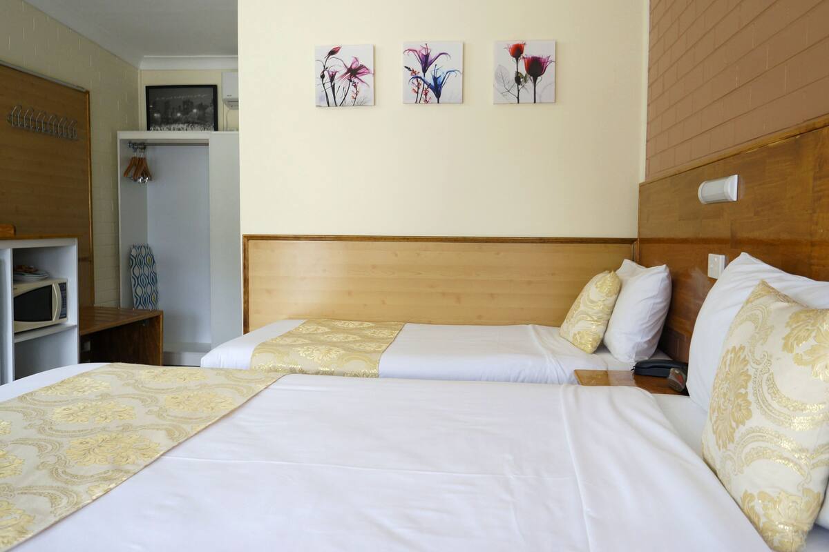 A hotel room with two beds, a wooden headboard, a microwave, and a small cabinet.