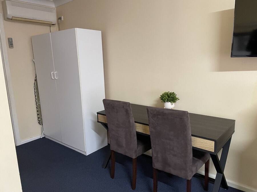 A small room with a dark wooden desk, two grey chairs, a white wardrobe, and a small potted plant on the desk.