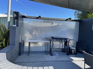 A patio area with a metal grill table, a lantern, and a gas cylinder. - Highway Motor Inn (Taree)