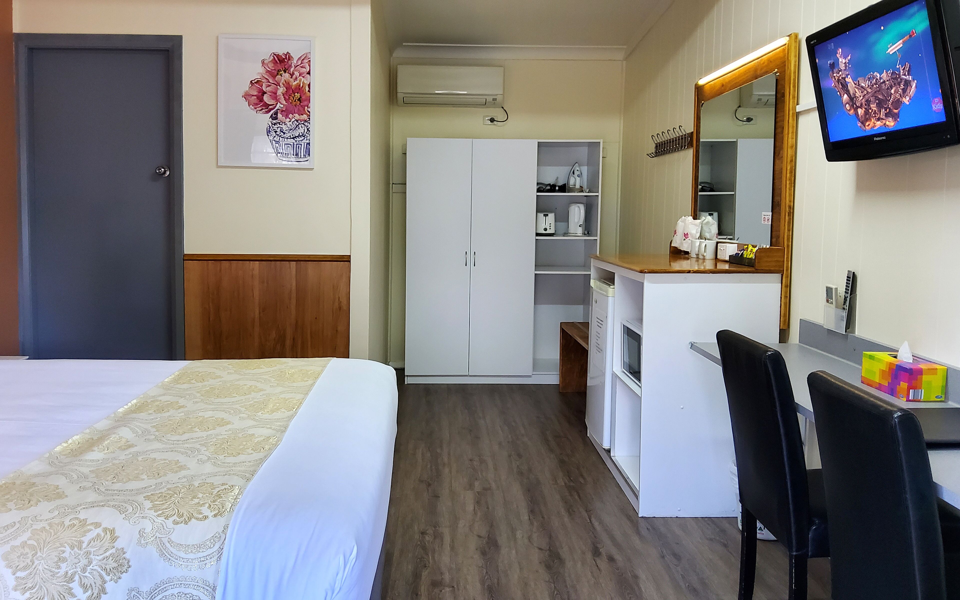 A hotel room with a bed, a desk with a chair, a wardrobe, a mirror, and a television.