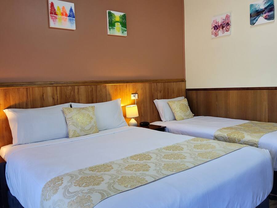 A hotel room with two beds, each with a white bedspread and gold trim, flanked by nightstands with lamps.