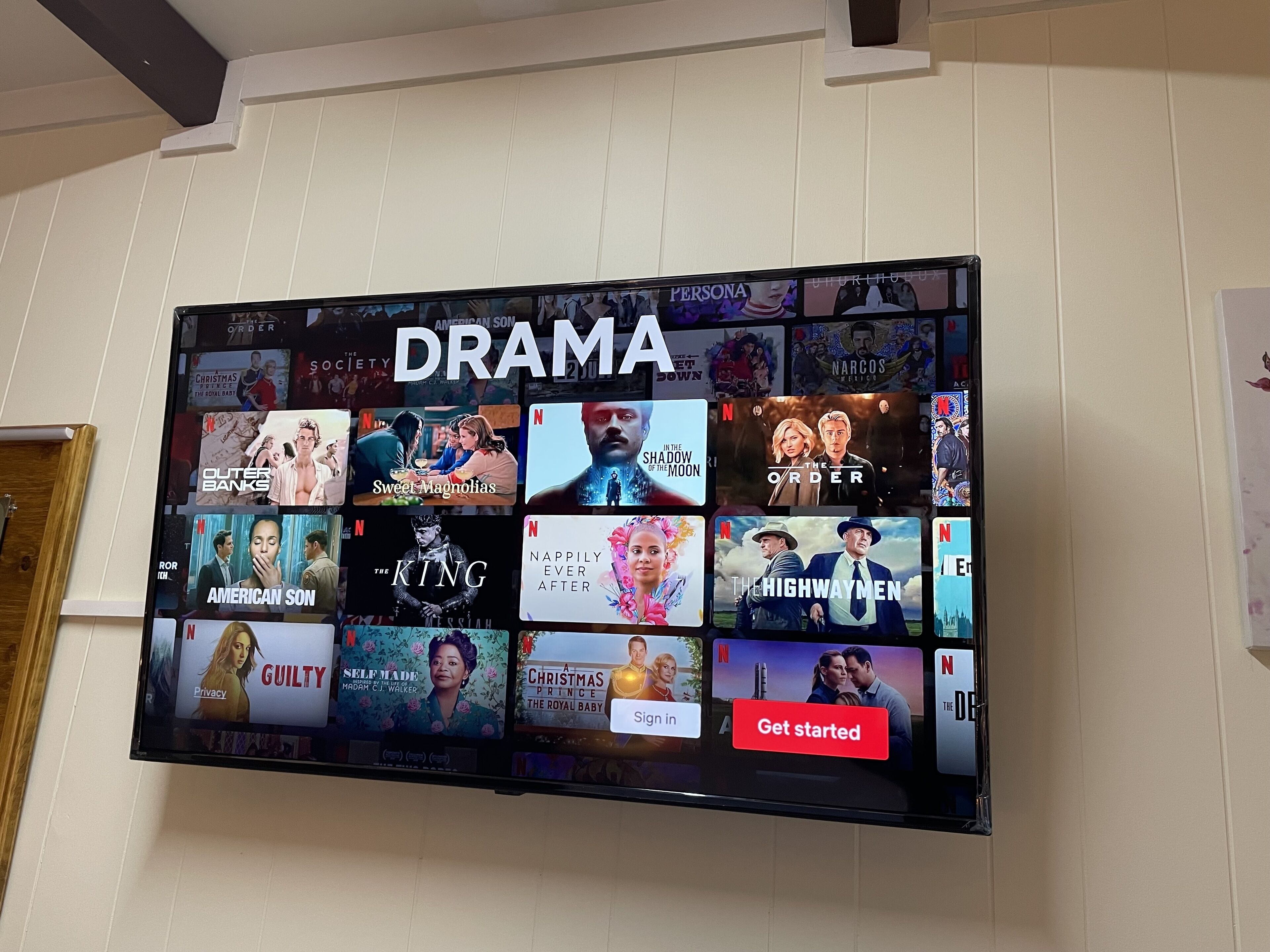 Un televisor de pantalla plana montado en la pared muestra diversas series dramáticas disponibles en Netflix.