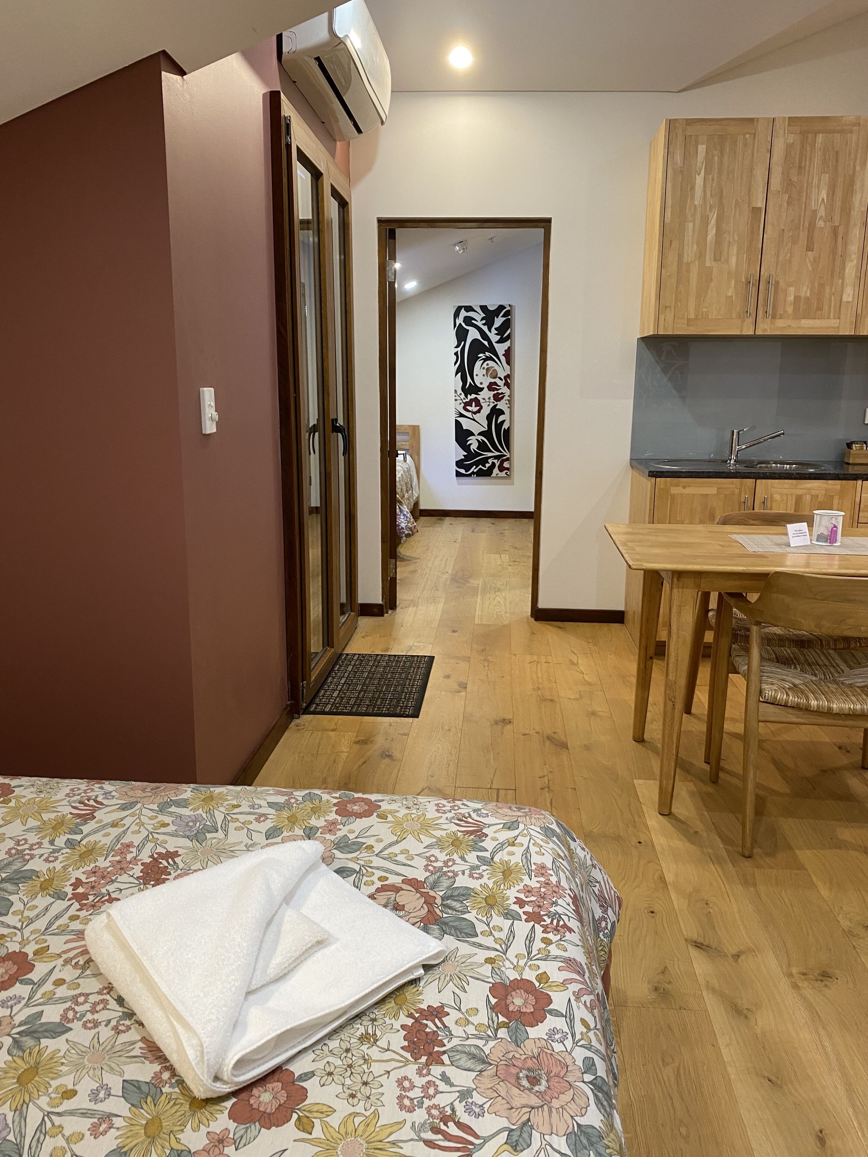 Una habitación de hotel con cama, escritorio de madera, kitchenette y puerta que da a otra habitación.
