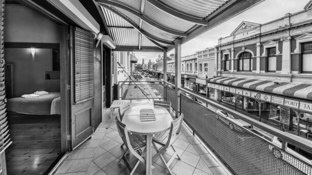 A balcony with a table and chairs, overlooking a street with historic buildings and a view of the port. - Rialto Suites (Fremantle)