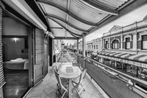 A balcony with a table and chairs, overlooking a street with historic buildings and a view of the port.