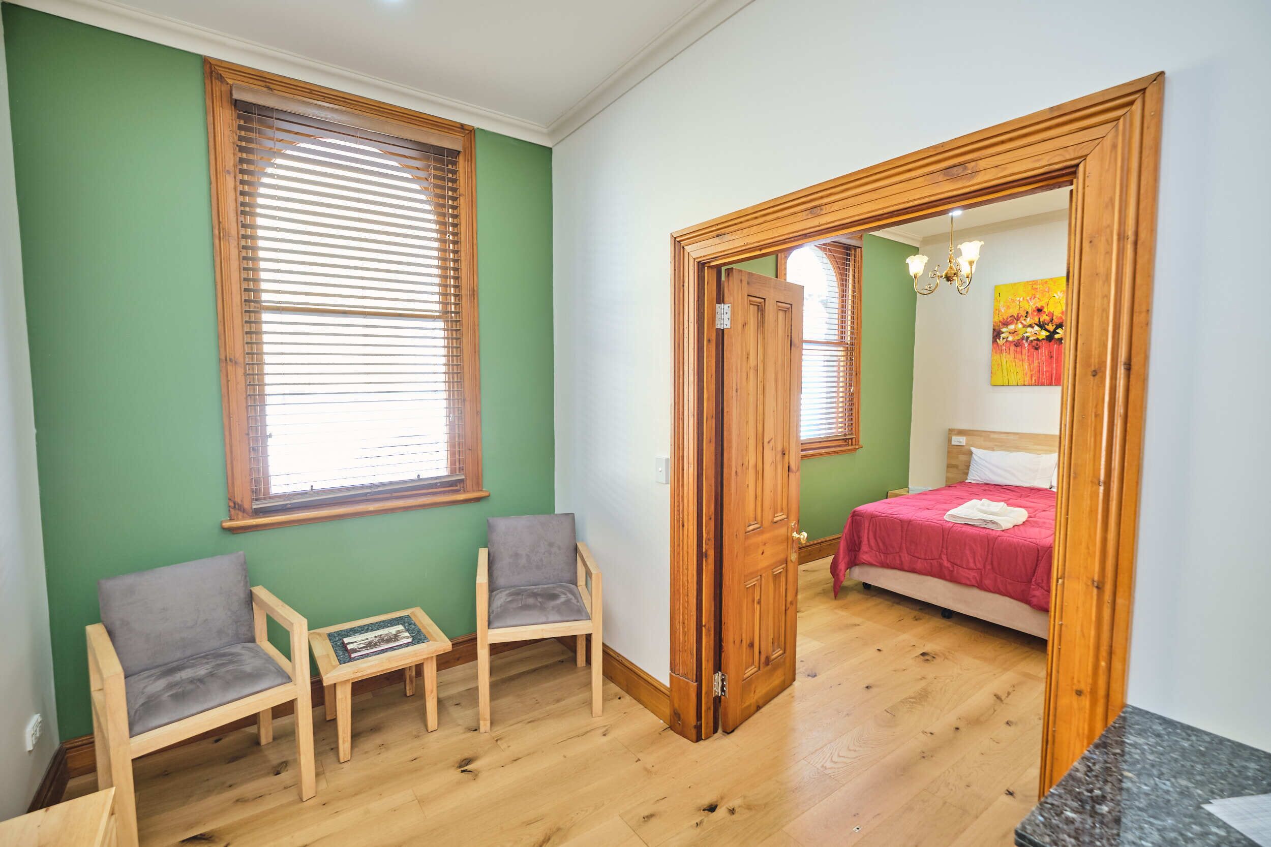 A room with a bed, two chairs, a small table, and a wooden door leading to another room.