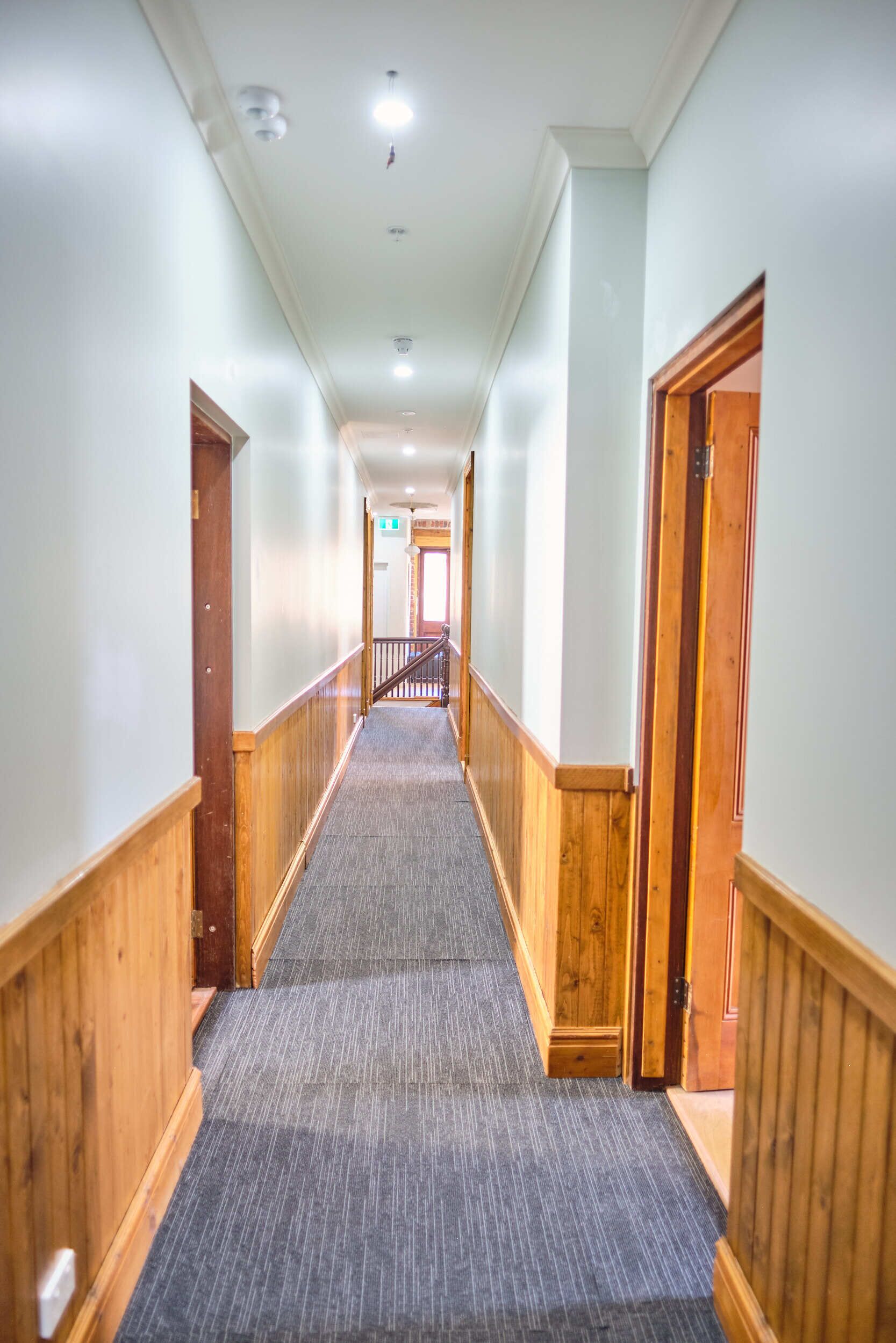 A long, narrow hallway with wooden paneling on the walls and carpeted floor, leading to a staircase with a wooden railing.