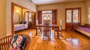A room with a wooden floor, a dining table with chairs, a bed with a headboard, and a window with blinds. - Rialto Suites (Fremantle)