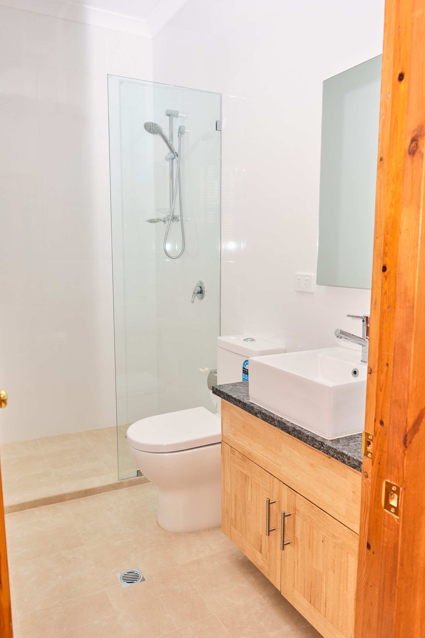 A bathroom with a glass-enclosed shower, a white toilet, a sink with a mirror, and wooden cabinets.