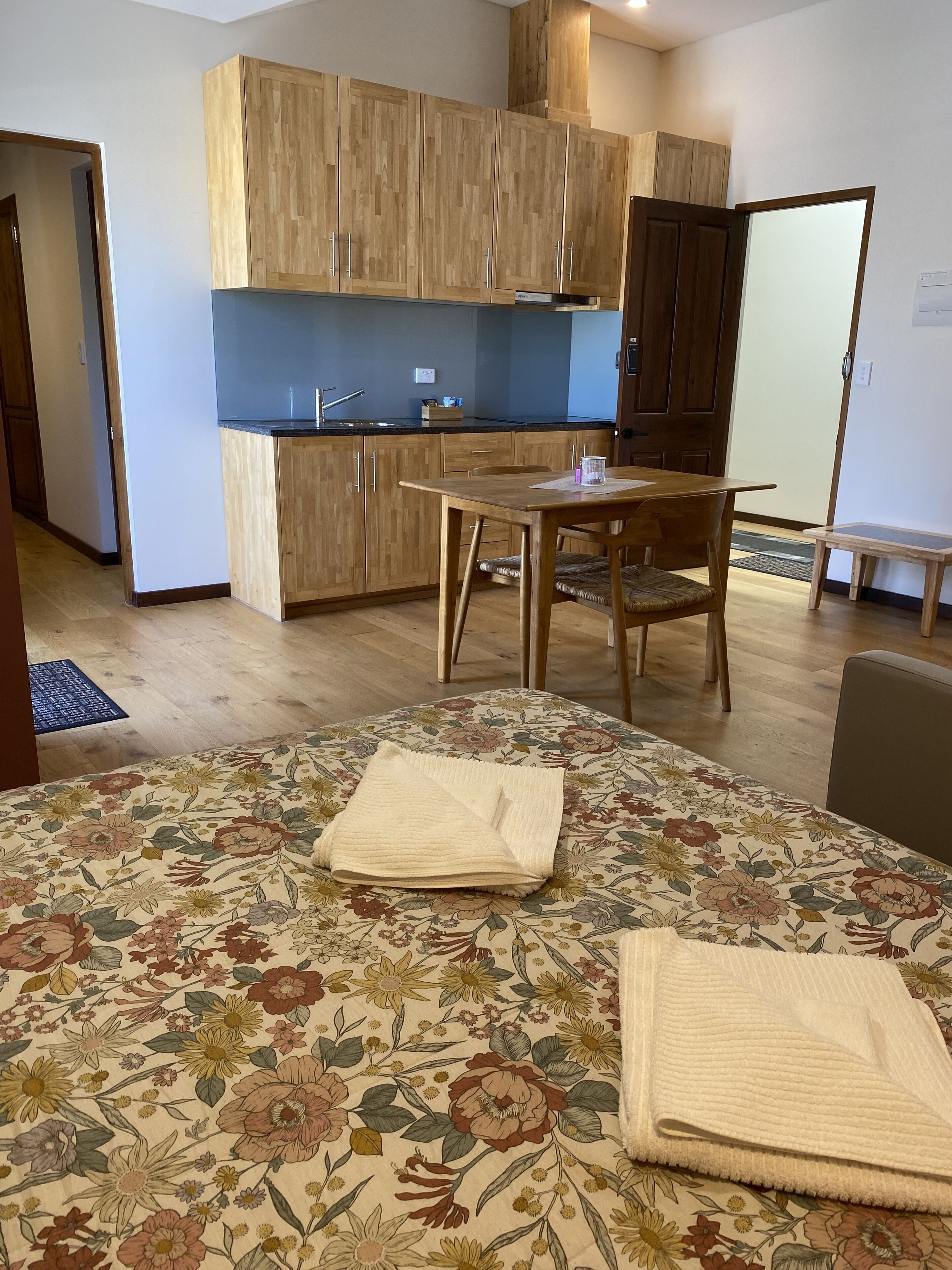 A modern kitchen with wooden cabinets, a dining table, and a floral-patterned area rug.