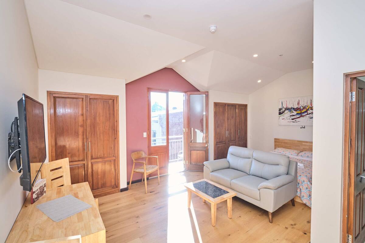 A spacious living area with a wooden dining table, a sofa, and a television.