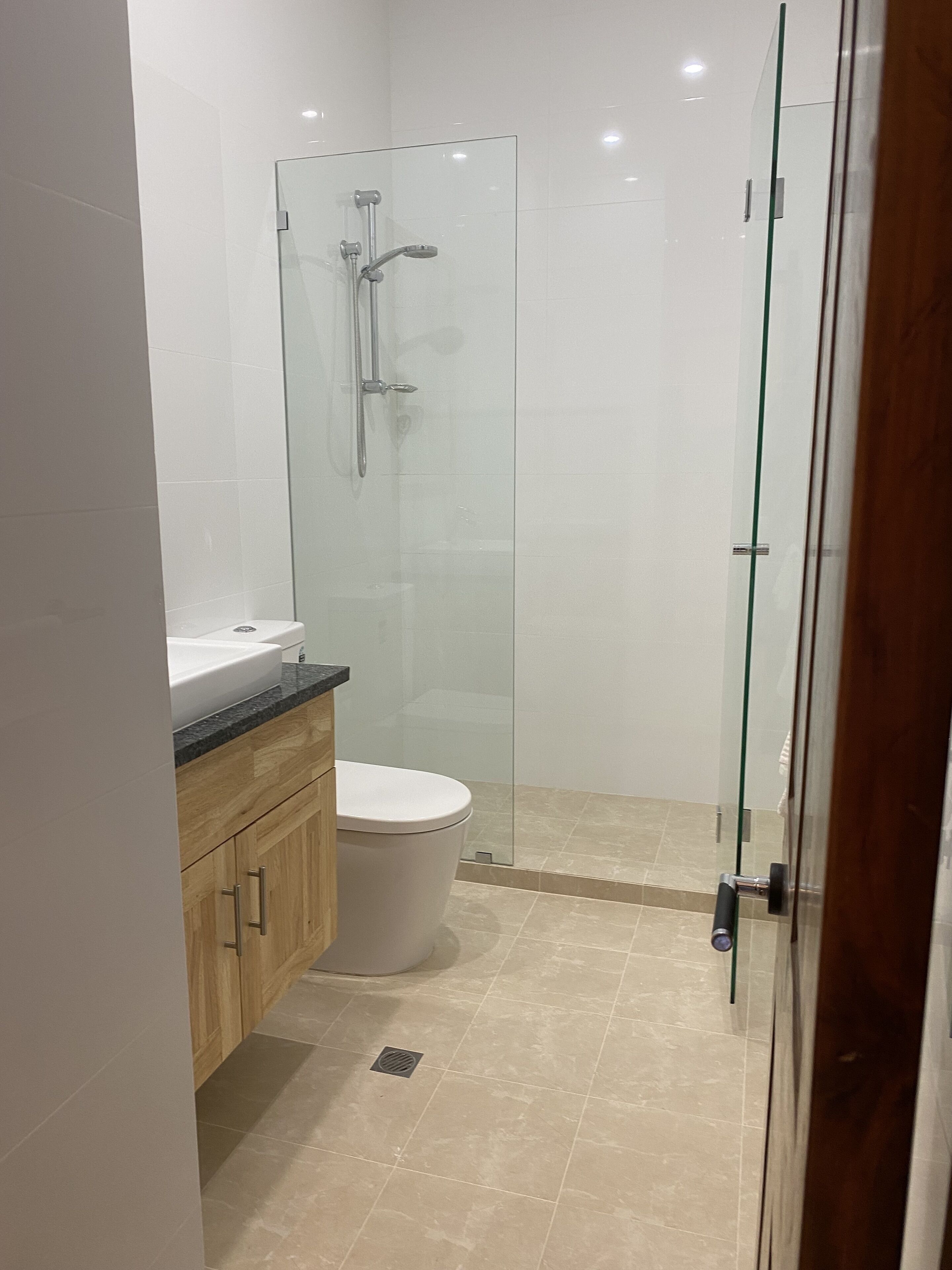 A modern bathroom with a glass shower enclosure, a white toilet, and wooden cabinets.