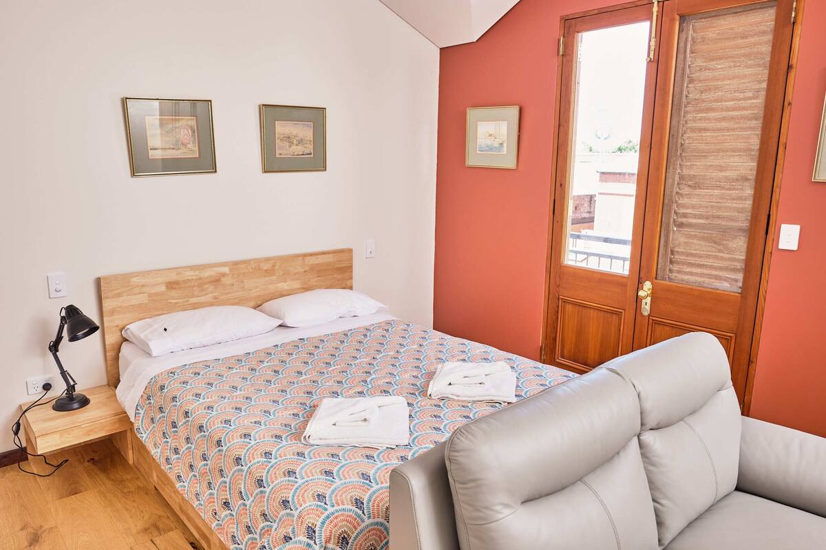 A neatly made bed with a patterned bedspread, a bedside lamp, and two framed pictures on the wall.