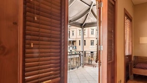A wooden door leading to a tiled patio with a metal gate, a bench, and a bed in the adjacent room. - Rialto Suites (Fremantle)