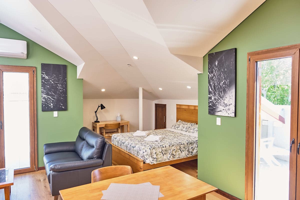 A bedroom with a bed, a sofa, a wooden table, and a desk.
