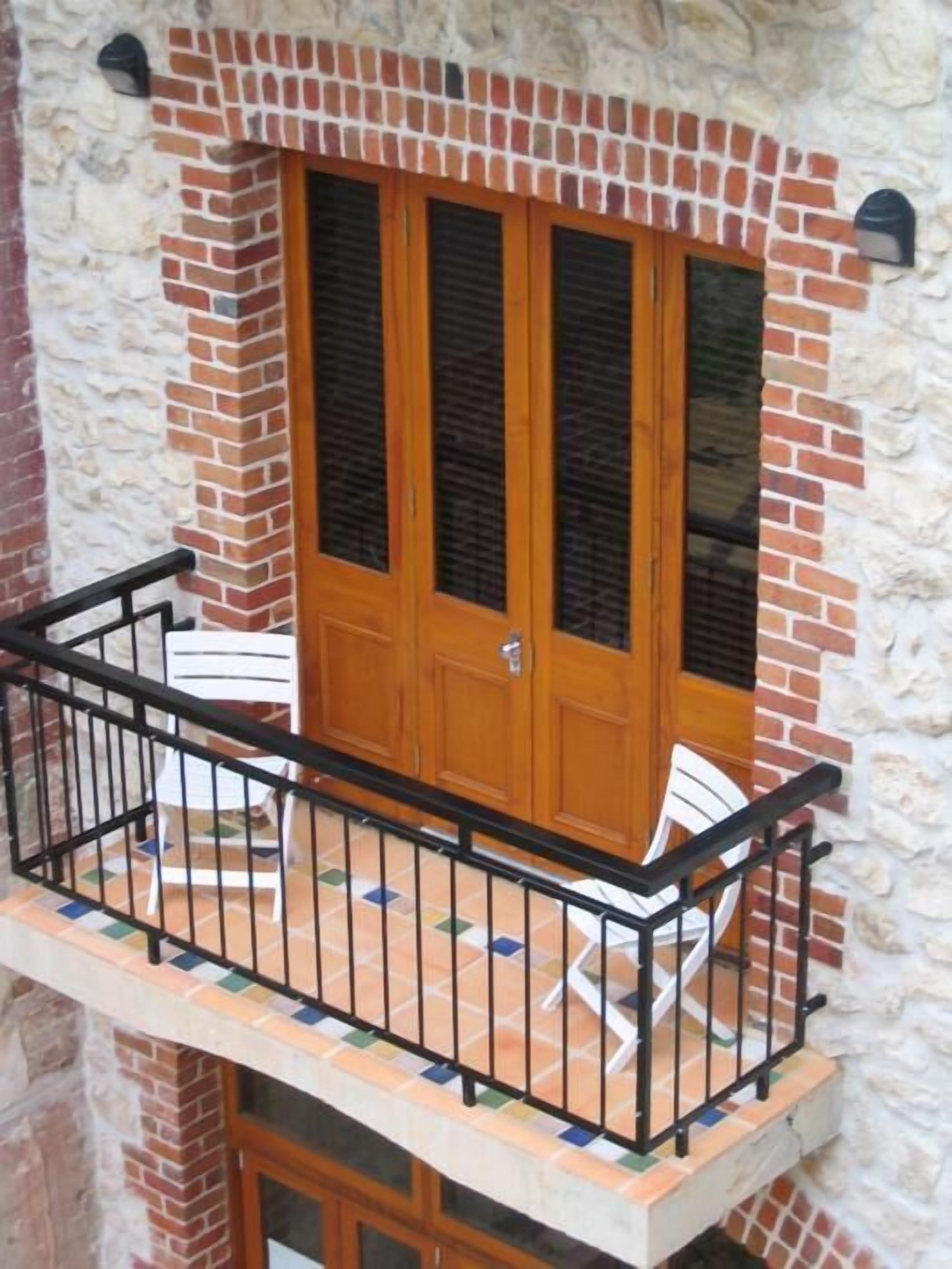 A balcony with a wooden door, a black metal railing, and two white chairs.