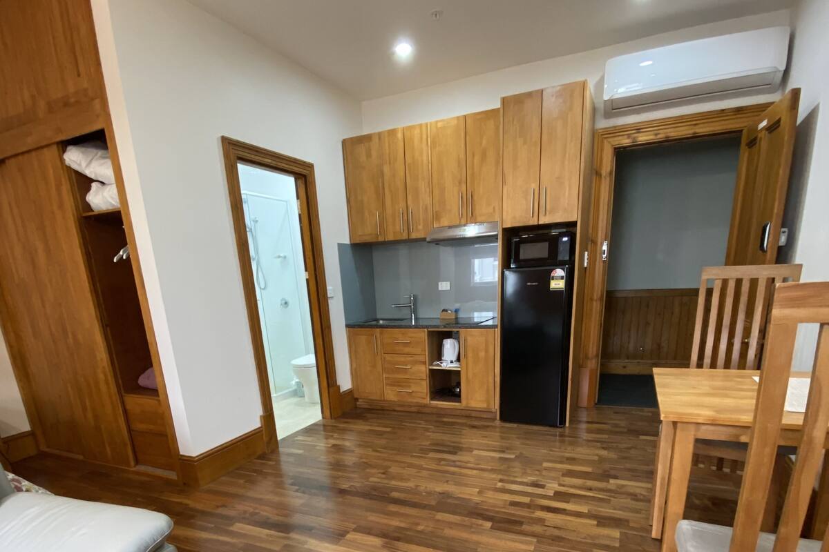 A spacious living area with a wooden floor, a sofa, a dining table with chairs, a kitchen with wooden cabinets, and a built-in oven.