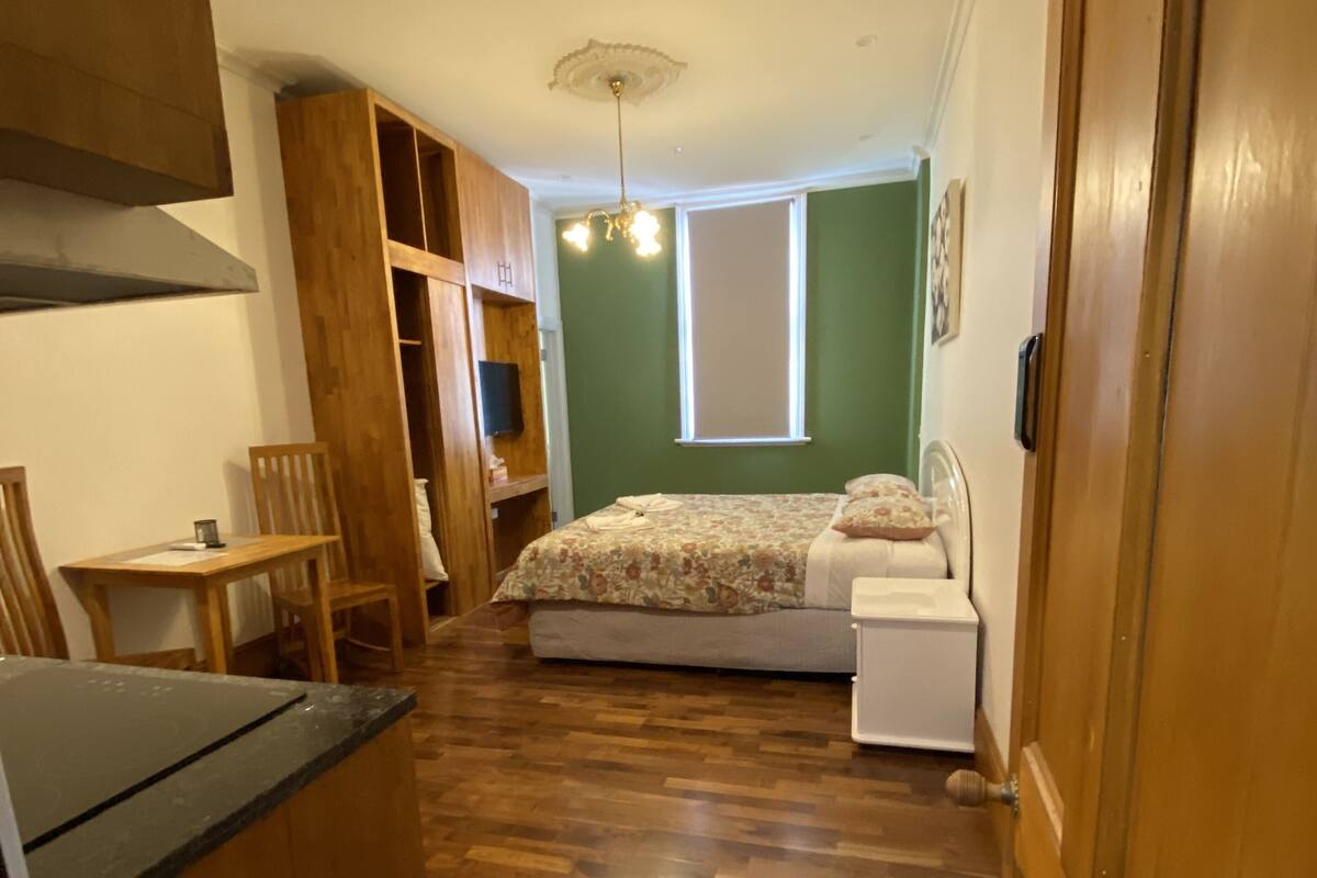 A narrow room with a bed, a small table, and a kitchenette.