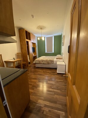 A narrow room with a bed, a small table, and a kitchenette.
