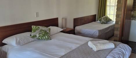 Habitación de hotel con dos camas, ventilador de techo, ventana con cortinas y pared de ladrillo.