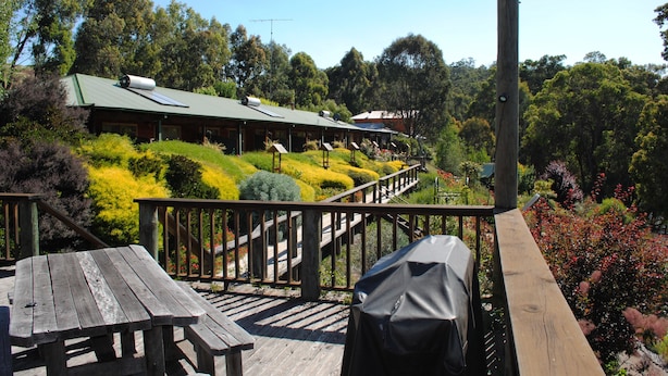 A wooden deck with picnic tables and a barbecue grill, overlooking a landscaped garden with a building in the background. - Tweed Valley Lodge (Bridgetown)