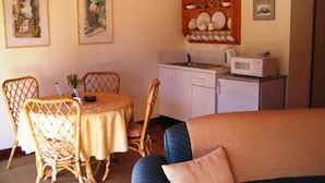 A cozy room with a dining table, chairs, a sofa, a kitchen area with a microwave, and a cabinet with dishes. - Tweed Valley Lodge (Bridgetown)