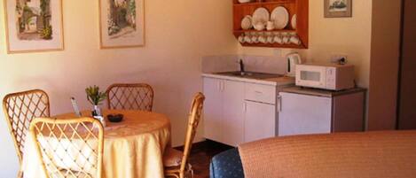 Una habitación acogedora con una mesa de comedor, sillas, un sofá, una zona de cocina con microondas y un armario con vajilla.