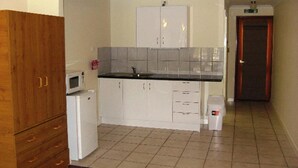 A compact kitchen with white cabinets, a microwave, and a tiled backsplash. - Tweed Valley Lodge (Bridgetown)