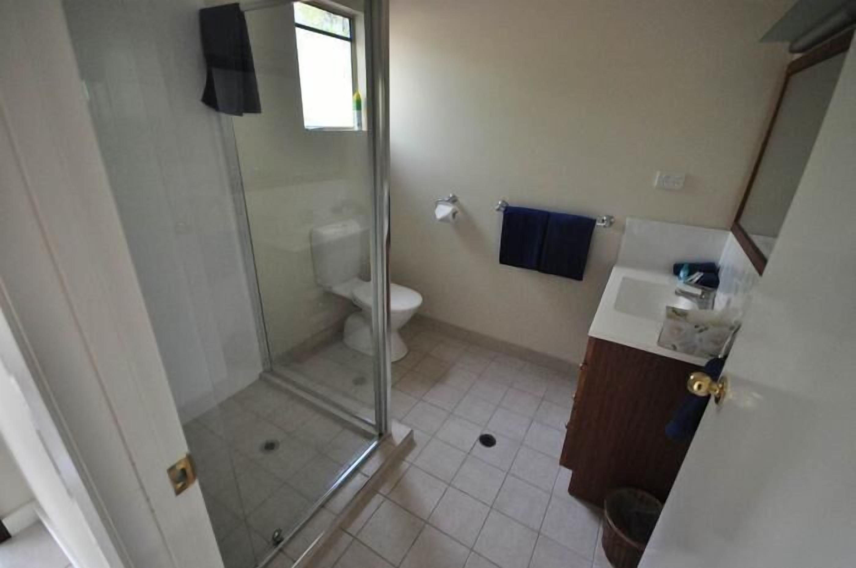 Un baño con cabina de ducha de vidrio, inodoro y lavamanos.