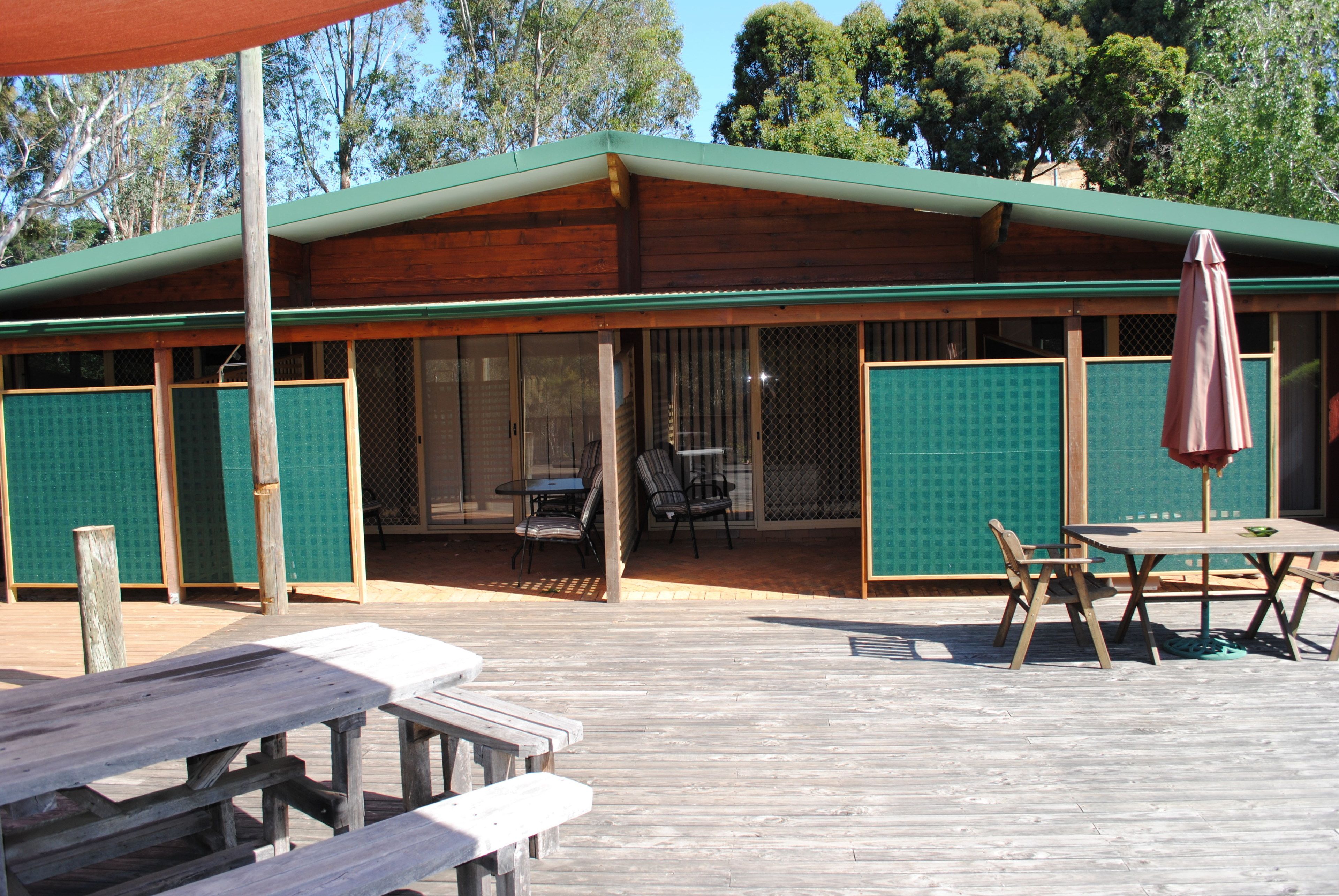 A wooden building with a covered patio area, featuring picnic tables and chairs, and a table with an umbrella.