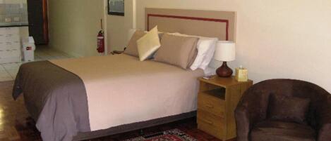 Una habitación de hotel con una cama, una mesita de noche con lámpara, una silla y una pequeña mesa.