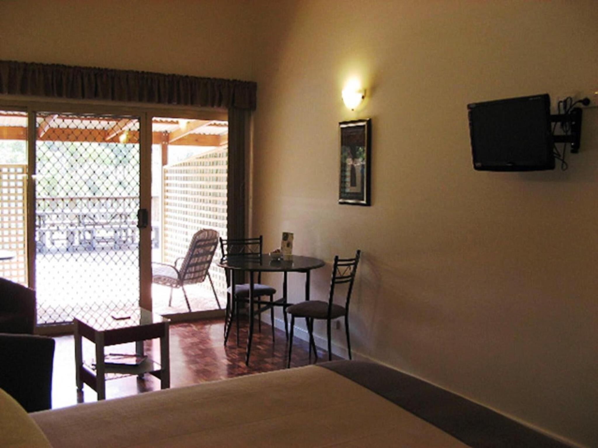 A room with a bed, a table with chairs, a TV mounted on the wall, and a door leading to an outdoor area.