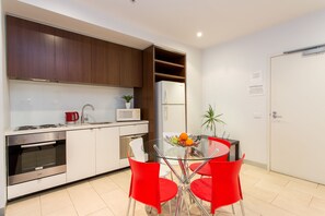 Une cuisine moderne avec des meubles blancs, des appareils en acier inoxydable et une table à manger en verre, assortie de chaises rouges.