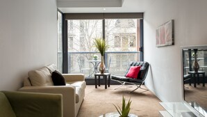 A modern living room with a sofa, a chair, a small table with a plant, and a large window offering a view of the outside. - ABC Accommodation - Flinders (Melbourne)