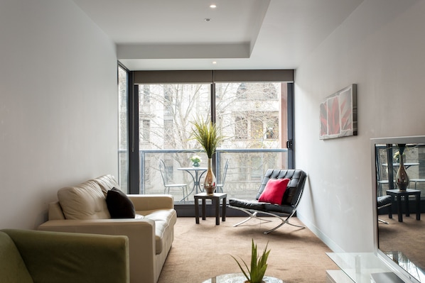 Ein modernes Wohnzimmer mit einer Couch, einem Sessel, einem kleinen Tisch mit einer Pflanze und einem großen Fenster mit Blick nach draußen.