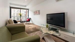 A modern living room with a flat-screen TV, green sofa, and a glass coffee table. - ABC Accommodation - Flinders (Melbourne)