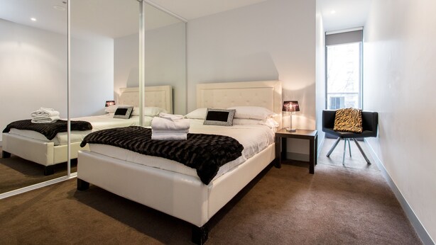 A modern bedroom with a large bed, a bedside table, a chair, and a mirror. - ABC Accommodation - Flinders (Melbourne)