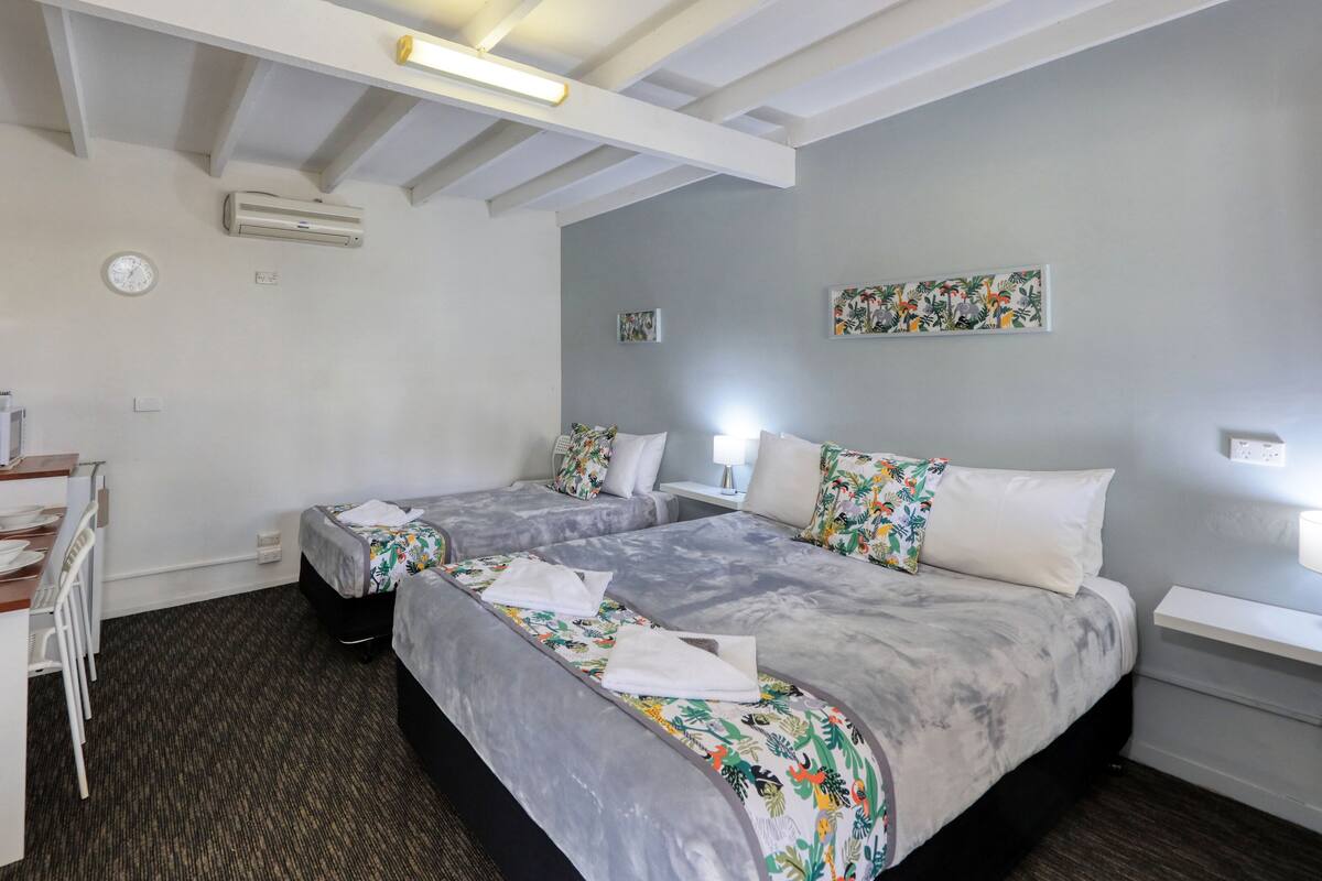 Une chambre d’hôtel avec deux lits, un bureau, un four à micro-ondes et une horloge murale.
