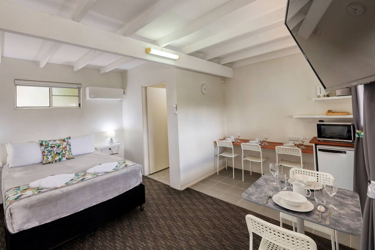 Une chambre d’hôtel comprenant un lit, une table de chevet, une lampe et un petit coin repas avec des chaises et une table.