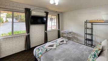 A hotel room with a bed, a small table with chairs, a TV mounted on the wall, and a window with curtains.