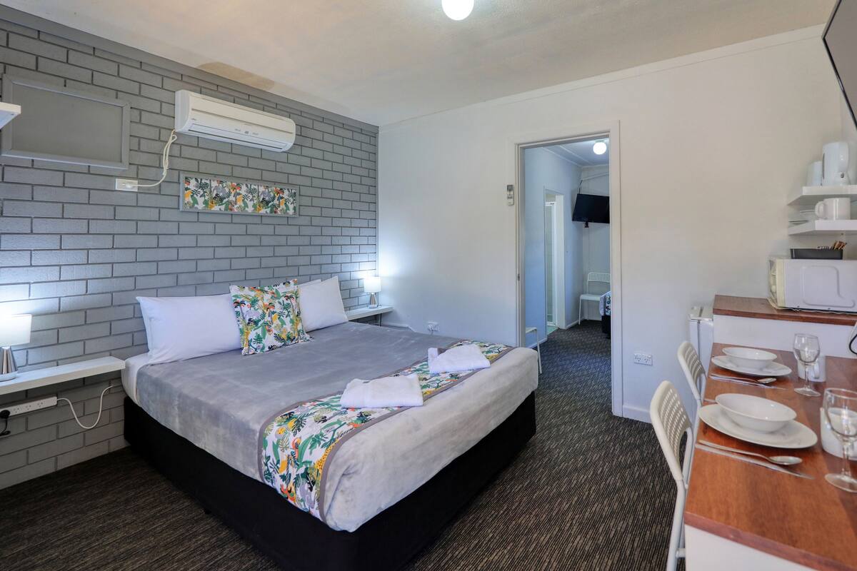 Une chambre d’hôtel équipée d’un lit, d’une table de chevet, d’une lampe, d’un climatiseur et d’un petit coin cuisine avec un four à micro-ondes et un grille-pain.