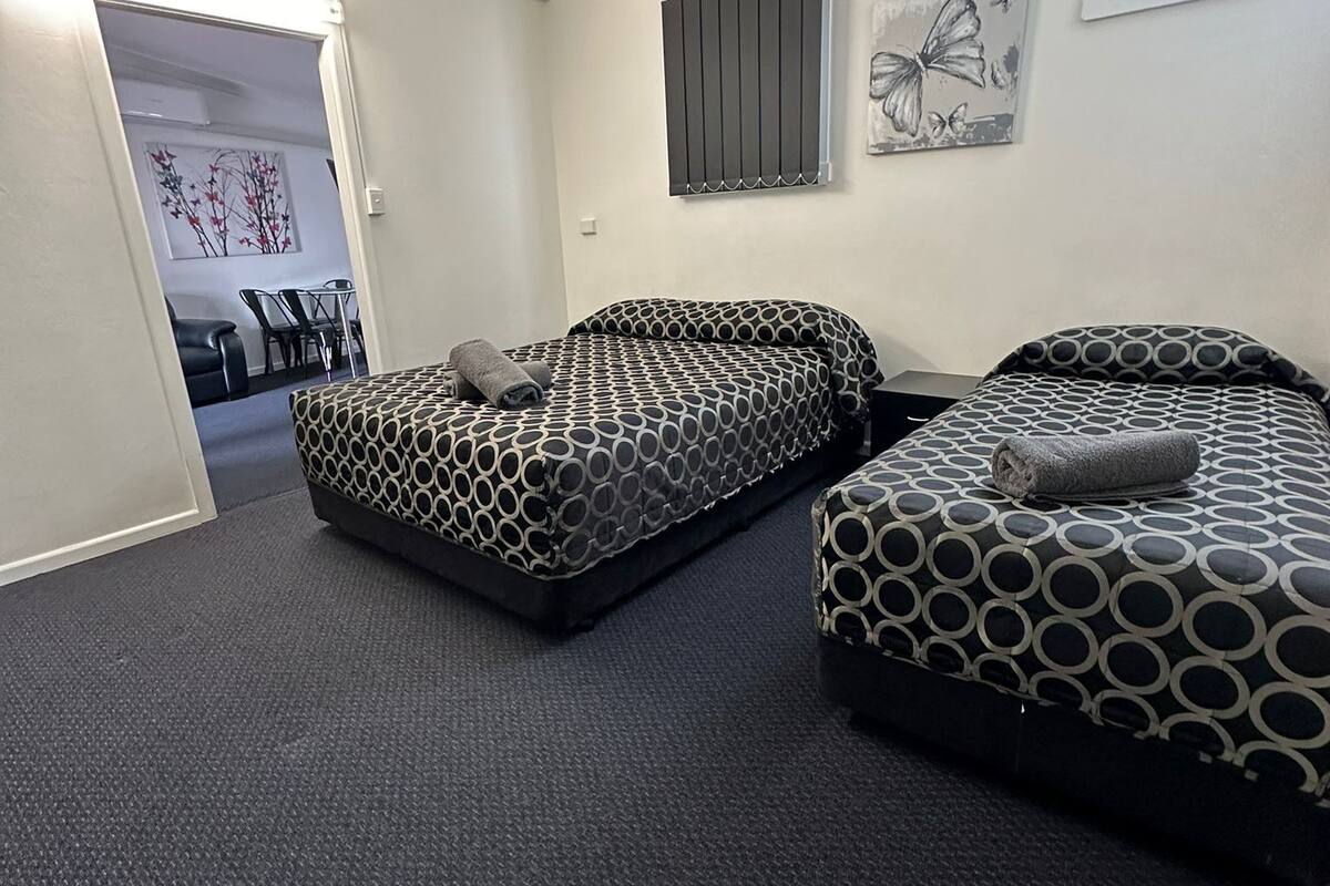 Quarto com duas camas, área de refeições e uma janela.