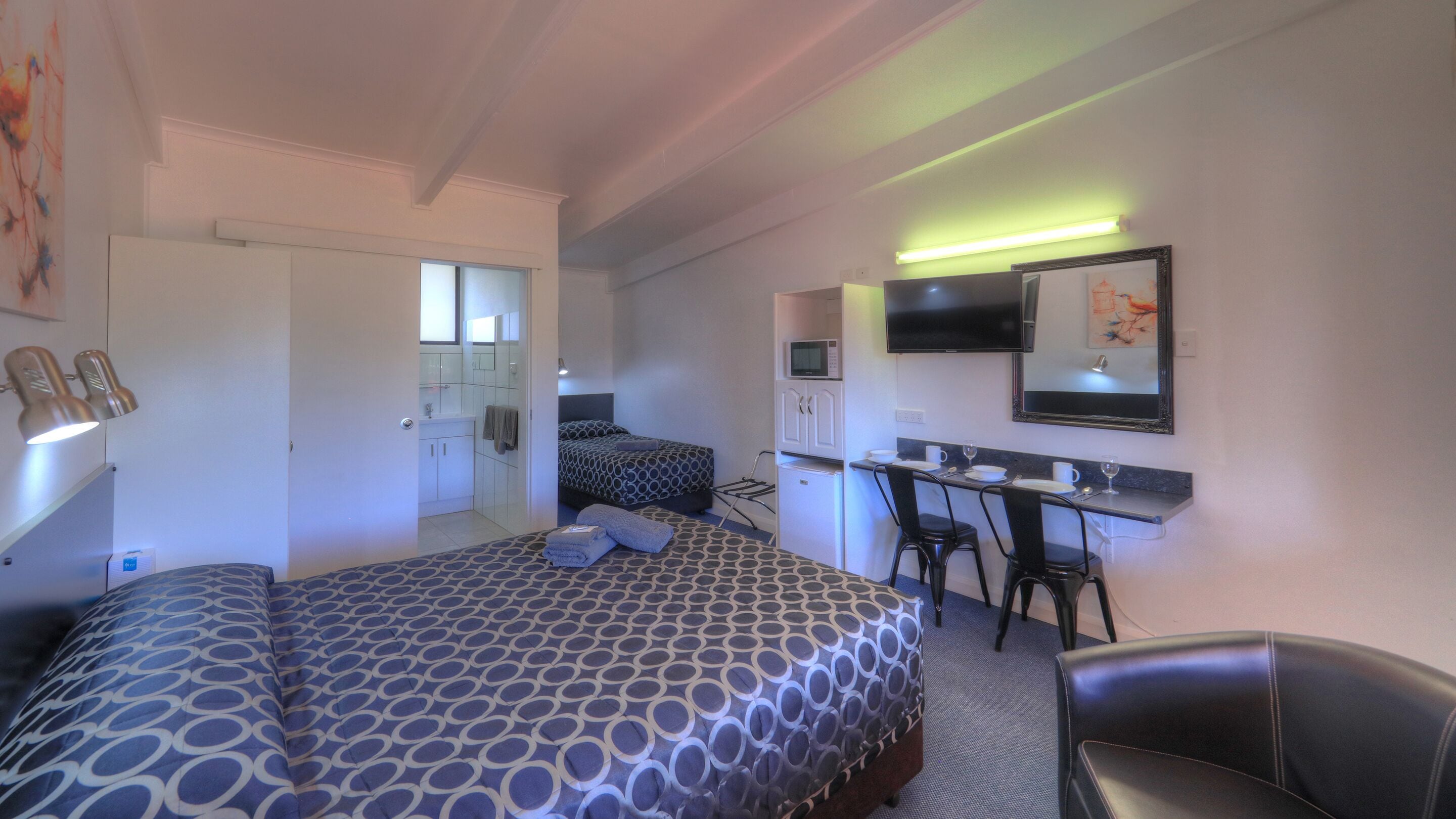 A hotel room with a bed, a desk, a chair, a TV, and a microwave.