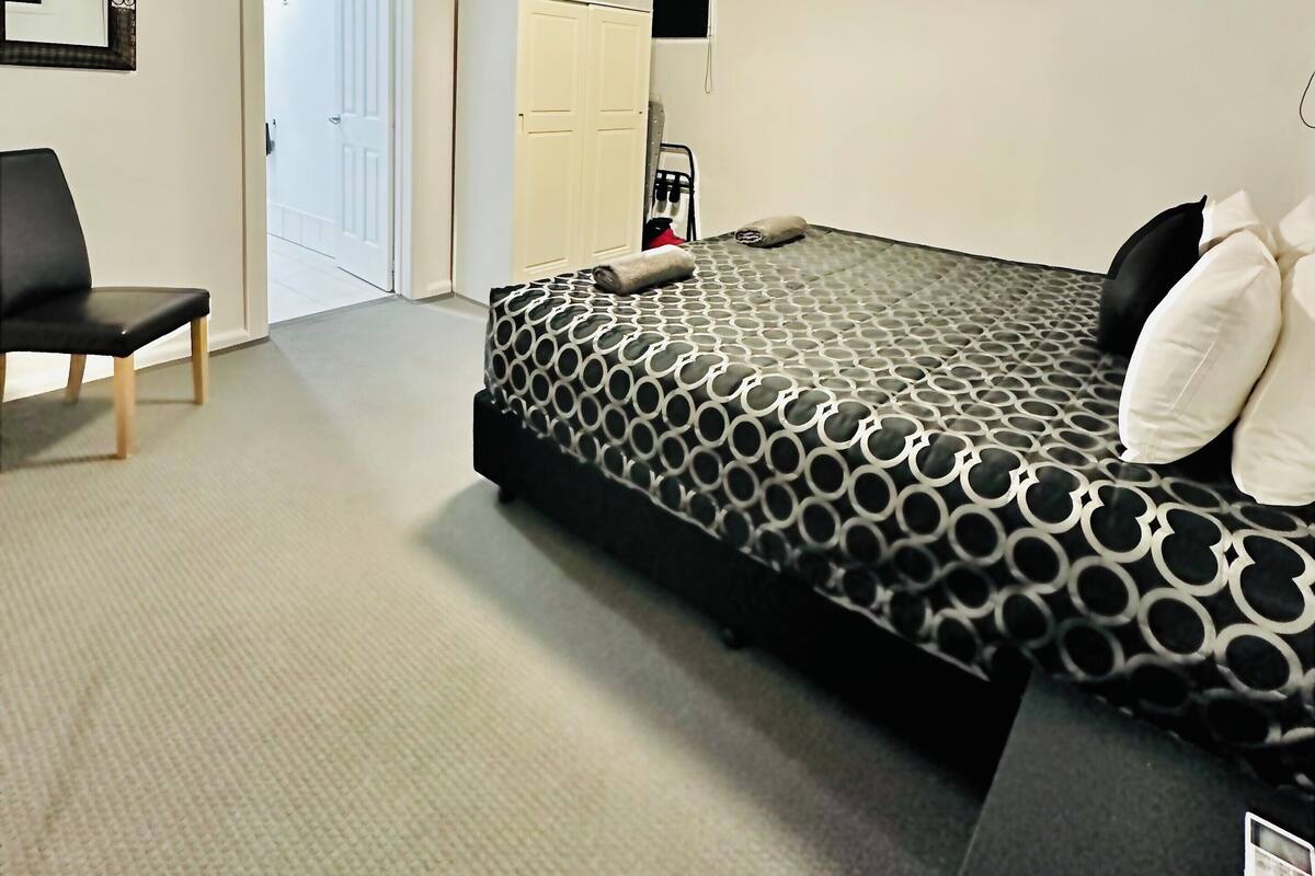 Quarto com cama, uma cadeira, guarda-roupa e porta para outro cômodo.
