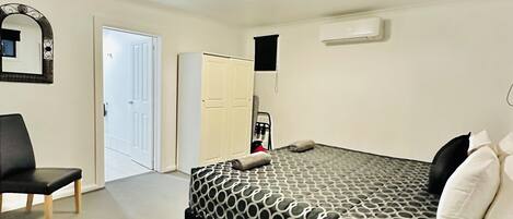 Un dormitorio con cama, una silla, un armario y una puerta que da a otra habitación.