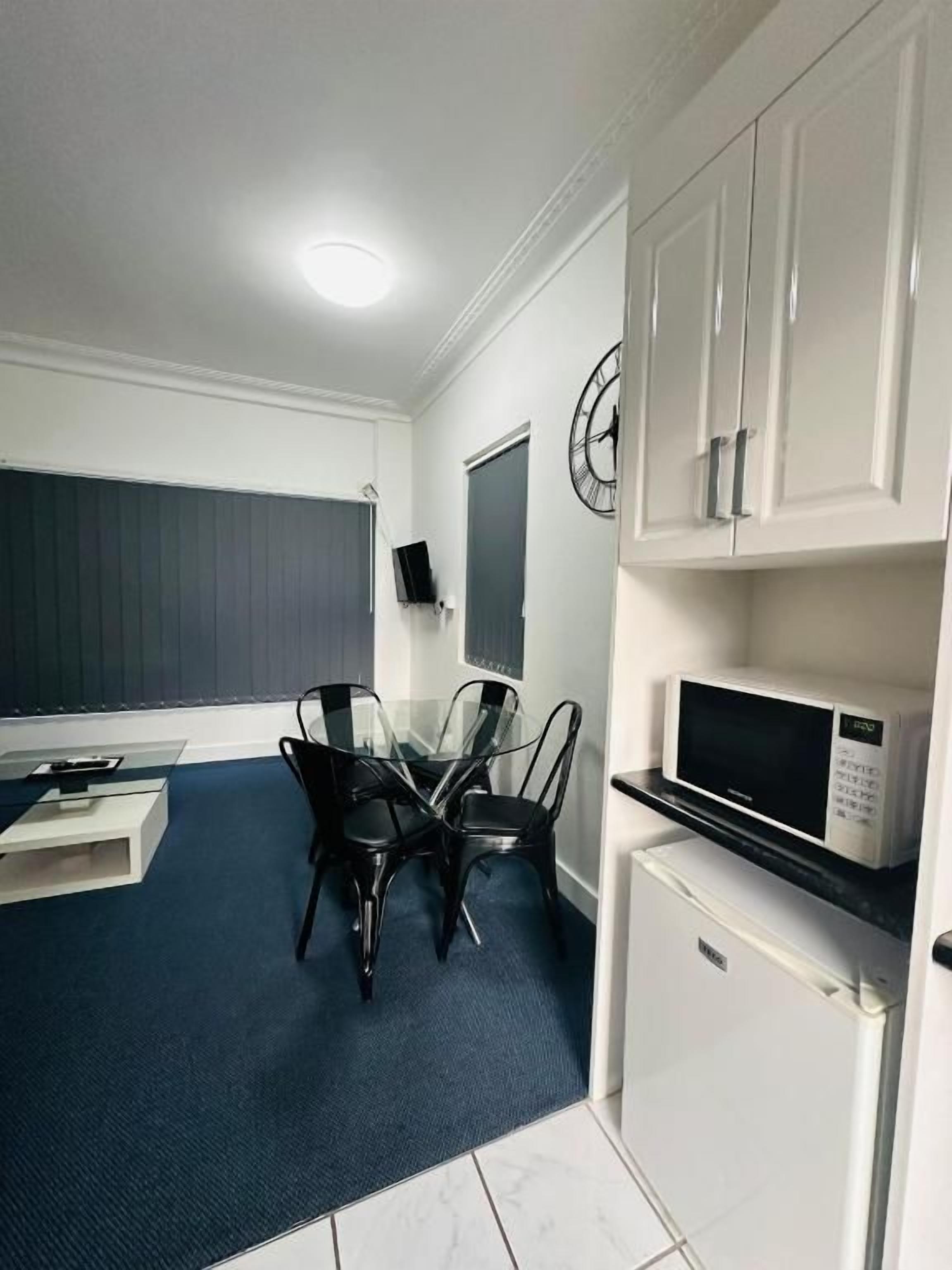 A compact kitchen with white cabinets, a microwave, and a dining area with a glass table and chairs.