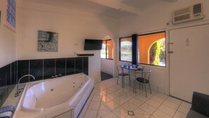 A modern bathroom with a large bathtub, a small table with chairs, and a window with a view of greenery. - Twin Swans Motel (Inverell)