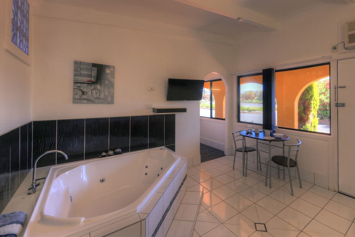 Uma casa de banho moderna com uma banheira grande, uma pequena mesa com cadeiras e uma janela com vista para o verde.