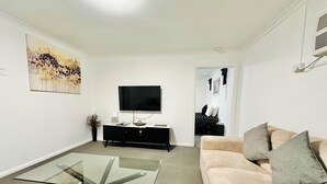 A modern living room with a glass-top coffee table, a beige sofa, a black entertainment unit, and a flat-screen TV. - Twin Swans Motel (Inverell)