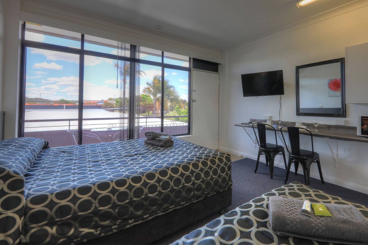 Quarto de hotel com cama, escrivaninha, televisão e micro-ondas.